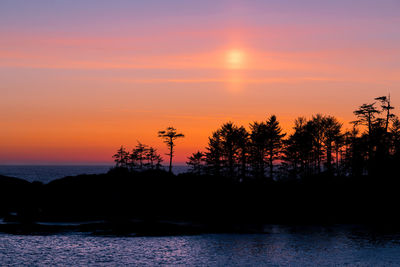 Silhouette trees by sea against romantic sky at sunset