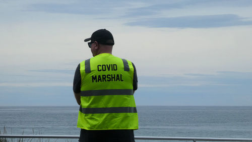 Rear view of man standing by sea against sky