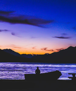 Silhouette man sitting on beach against sky during sunset