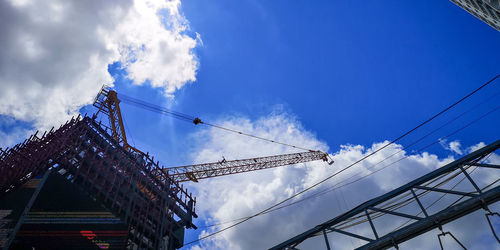 Low angle view of crane by building against sky