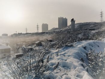 Snow covered buildings against sky during sunset