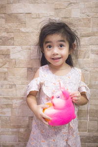 Portrait of cute girl holding pink face against wall