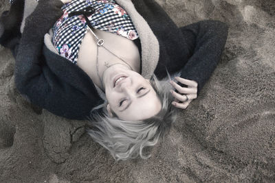 High angle view of smiling young woman wearing chain with key pendant while lying on sand at beach