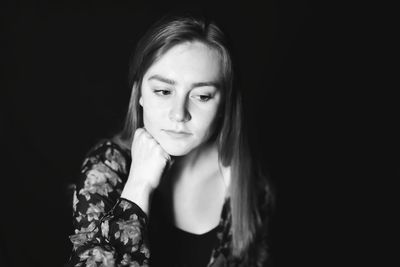 Close-up of thoughtful young woman with hand on chin against black background