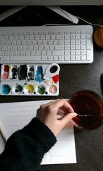 Woman stirring tea with art equipment and computer keyboard on table