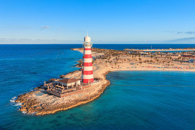 Lighthouse by sea against blue sky