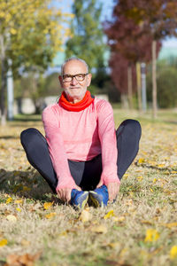 Portrait of senior man exercising while sitting on grassy field at park