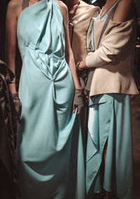 Two cropped female fashion figures in blue and beige stylish outfits, long dress and jacket 