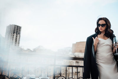 Young woman wearing sunglasses standing against railing in city