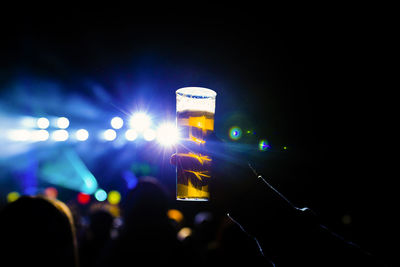 Cropped hand holding beer glass at concert during night