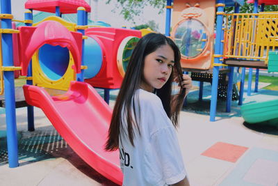 Portrait of teenage girl standing against play equipment at park
