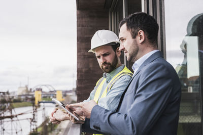 Architect explaining building contractor over tablet pc by railing