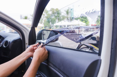 Cropped hands of woman removing plastic from car window