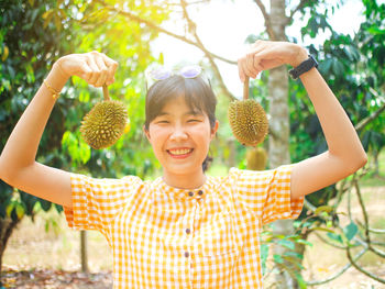 Portrait of smiling young woman holding durians at farm