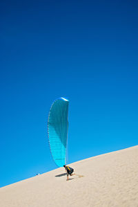 Low angle view of umbrella on sand against clear blue sky