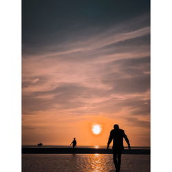 Silhouette people standing by sea against sky during sunset