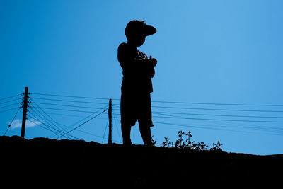 Low angle view of silhouette boy standing against clear blue sky