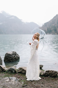 Beautiful young woman bride in a boho dress and with an umbrella stands in the rain in nature