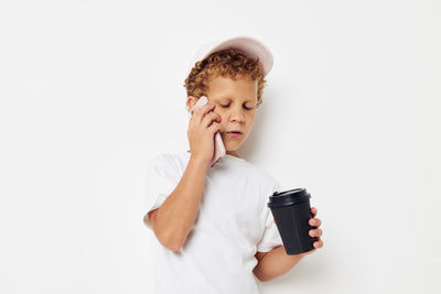 Boy talking on phone while holding coffee cup against white background