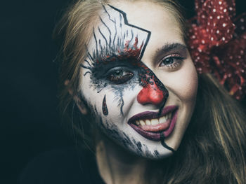 Close-up portrait of smiling woman with painted face against black background