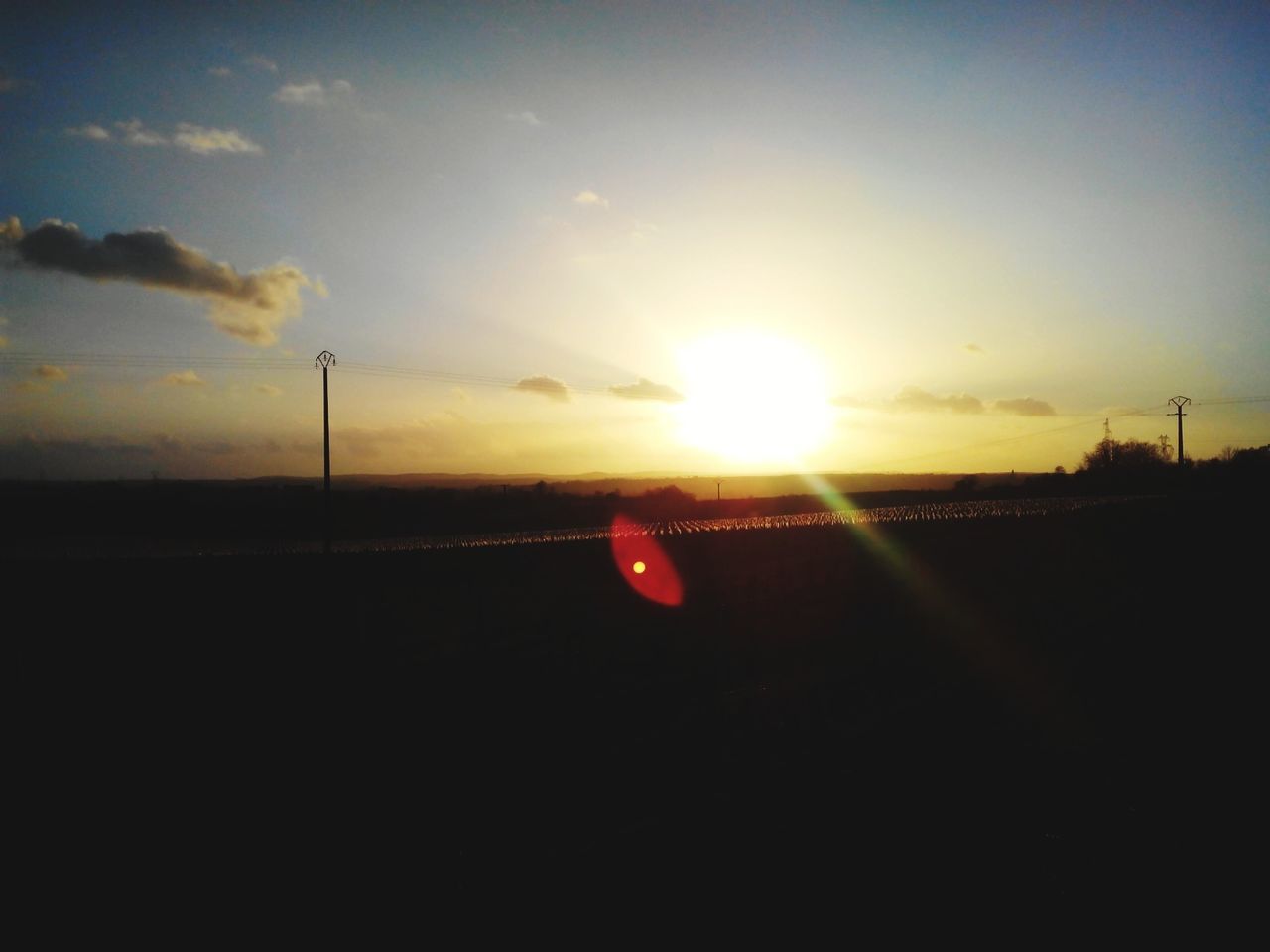 sunset, sun, transportation, silhouette, sky, orange color, lens flare, street light, sunlight, road, sunbeam, connection, nature, tranquility, scenics, beauty in nature, outdoors, no people, electricity pylon, cloud - sky