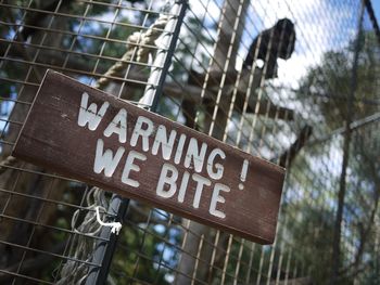 Low angle view of warning sign on metal fence in zoo