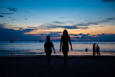 Silhouette people on beach against sky during sunset