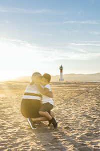 Full length of grandfather with grandson on beach against sky during sunset