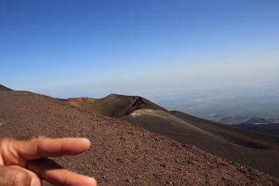 Cropped hand of person at mount etna against sky