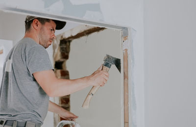 A young caucasian male builder is working with an ax in a doorway.