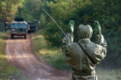 Rear view of male army soldier in protective workwear gesturing against trucks