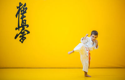 Portrait of cute boy practicing martial arts against yellow wall