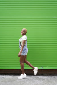 Full length portrait of a girl standing against green wall