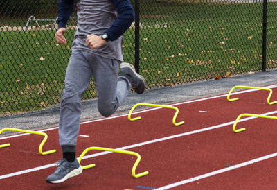 A high school boy running over small hurdles on a track during track running practice outside.