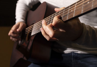 Closeup white man plays guitar, holding musical instrument in hands, sitting on chair in studio