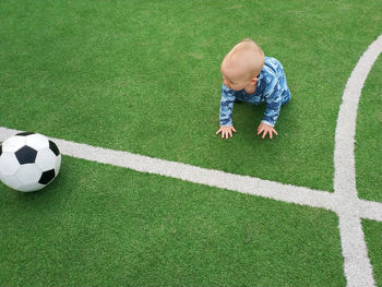 High angle view of cute baby boy with ball siting on soccer field