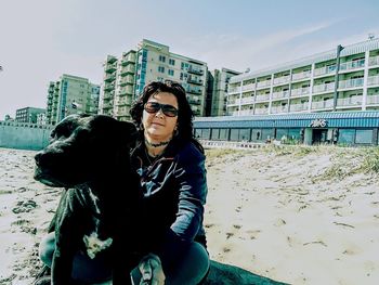 Young woman with dog on sand in city against sky