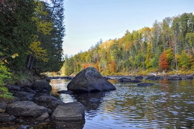 Rocks by river against sky during autumn