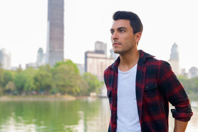 Young man looking away while standing against buildings