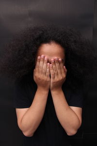 Woman covering face with hand against wall