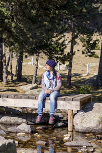 Full length of woman sitting on boardwalk against trees in forest