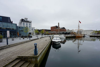 Sailboats moored at harbor by buildings against sky