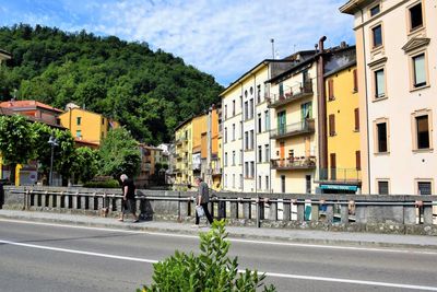 People walking on road by buildings in city against sky