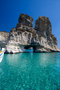 Scenic view of rock formation in sea against clear blue sky