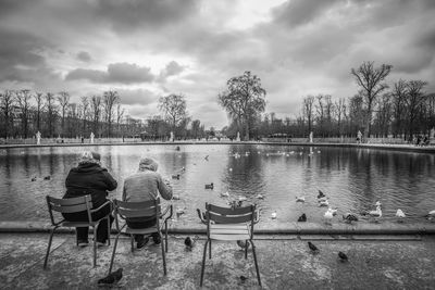 Rear view of people sitting on chair by lake