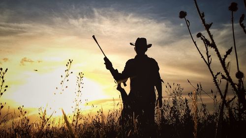 Man holding rifle while standing amidst plants against sky