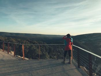 Rear view of woman standing on footbridge against cloudy sky