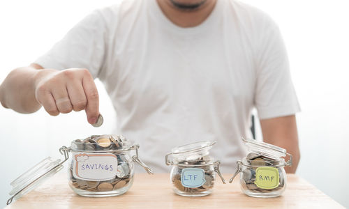 Midsection of man putting coin in jar against white background