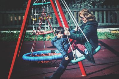 Side view of grandmother with grandson sitting on swing at playground