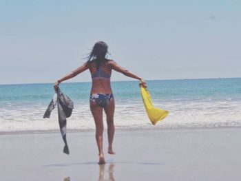 Rear view of young woman walking on beach against clear sky